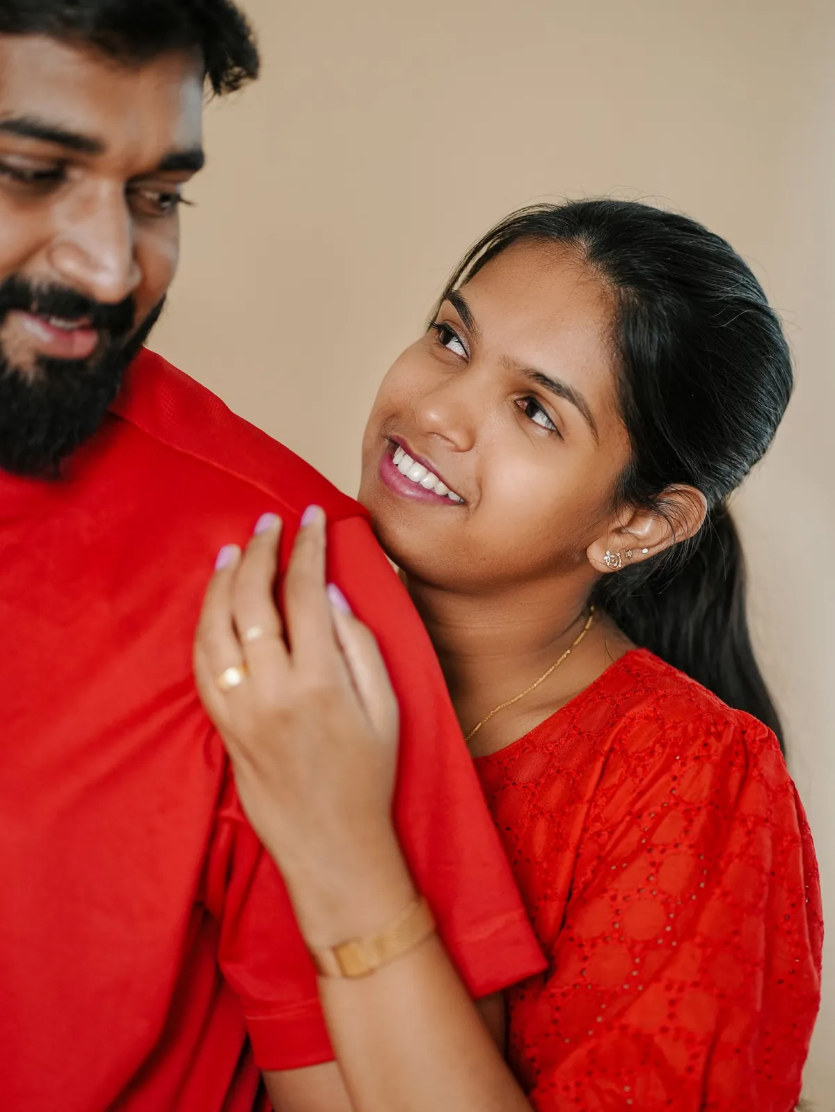 A woman in red rests her hand on her partner's shoulder and smiles up at him; he is in soft focus in the foreground.
