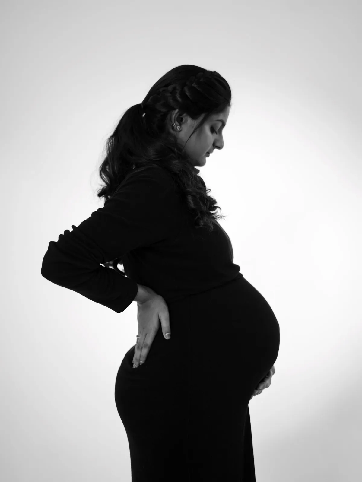 Black and white profile of a pregnant woman against a glowing white background, one hand at her back and the other under her bump.