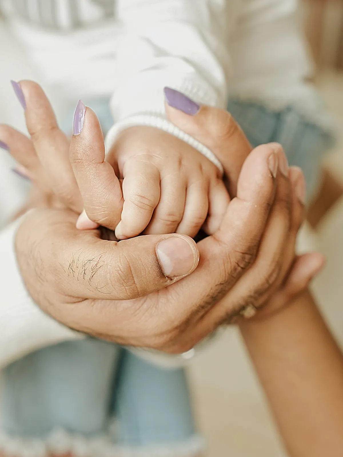 A baby's hand resting inside the cupped hands of both parents, photographed close.