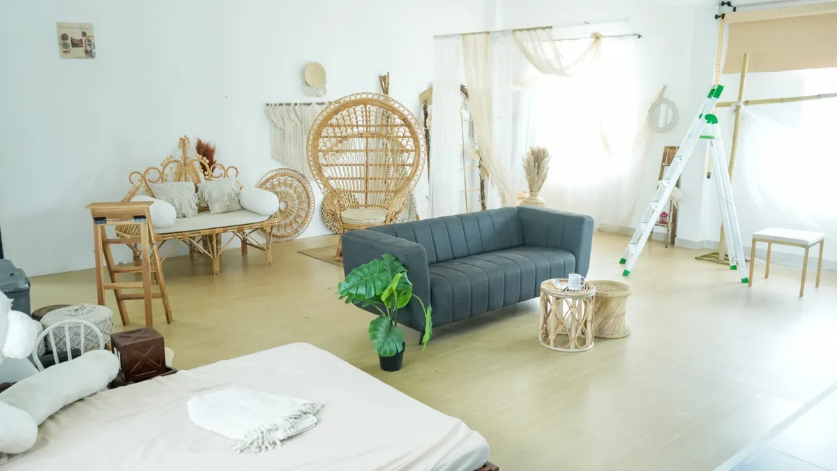 A bright white room styled with a rattan peacock chair and bench, macramé, pampas, sheer curtains, a grey sofa and a low bed.