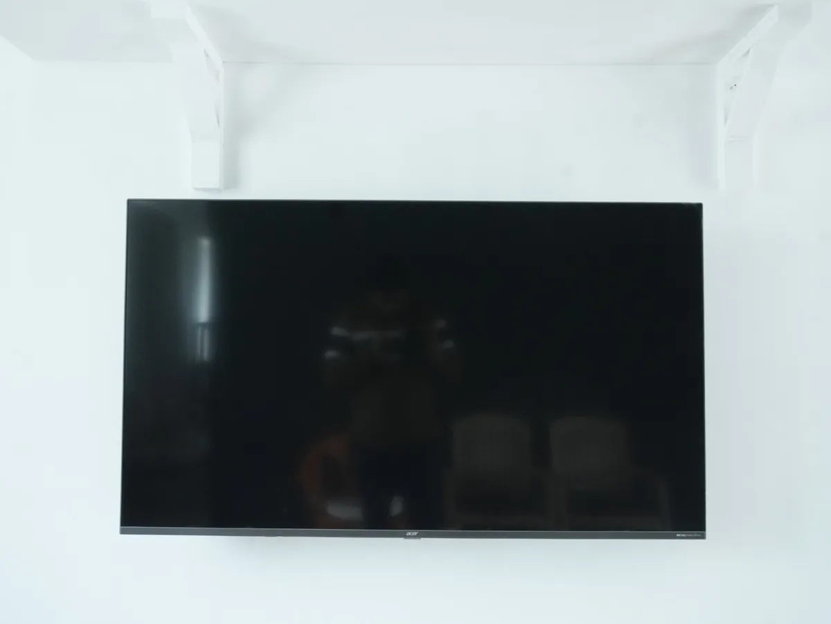 A wall-mounted television on a white wall beneath a shelf.