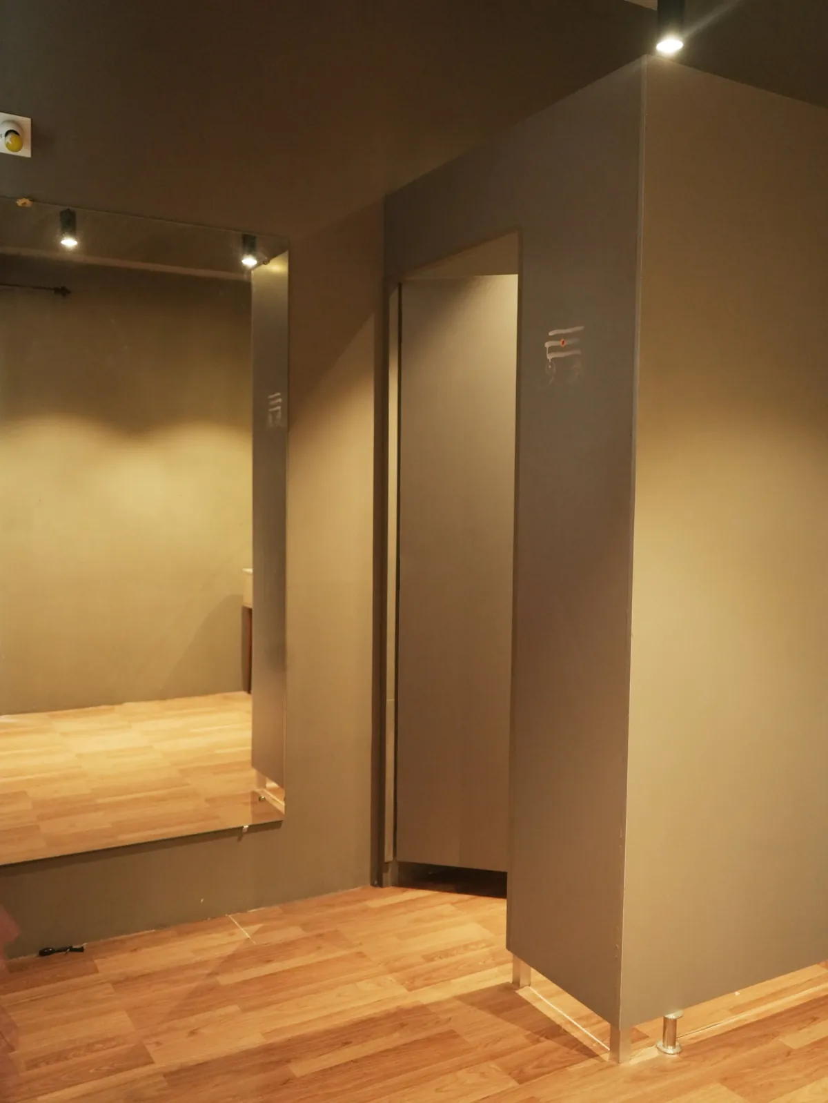 The changing room: a private cubicle beside a full-length wall mirror, with wooden flooring and warm spot lighting.